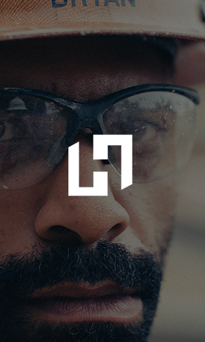 Close-up of a builder in safety glasses and a hard hat with the white Howell H monogram